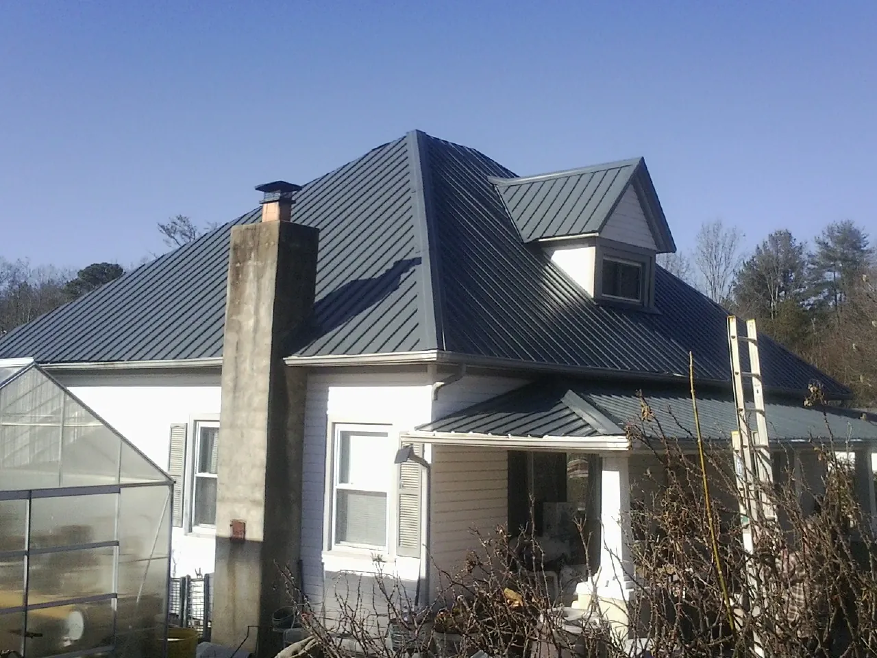 Dark blue standing seam metal roof on a white farmhouse with dormer — Slate & Tile Roof Repair by Roofing Brothers in West Chazy