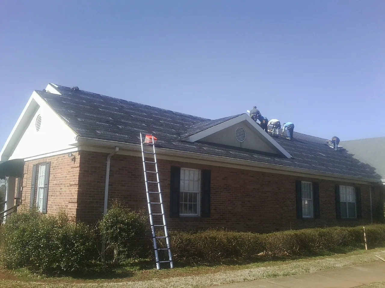 Crew tearing shingles off a brick ranch roof with a ladder set — Metal Roof Repair work by our crew in West Chazy