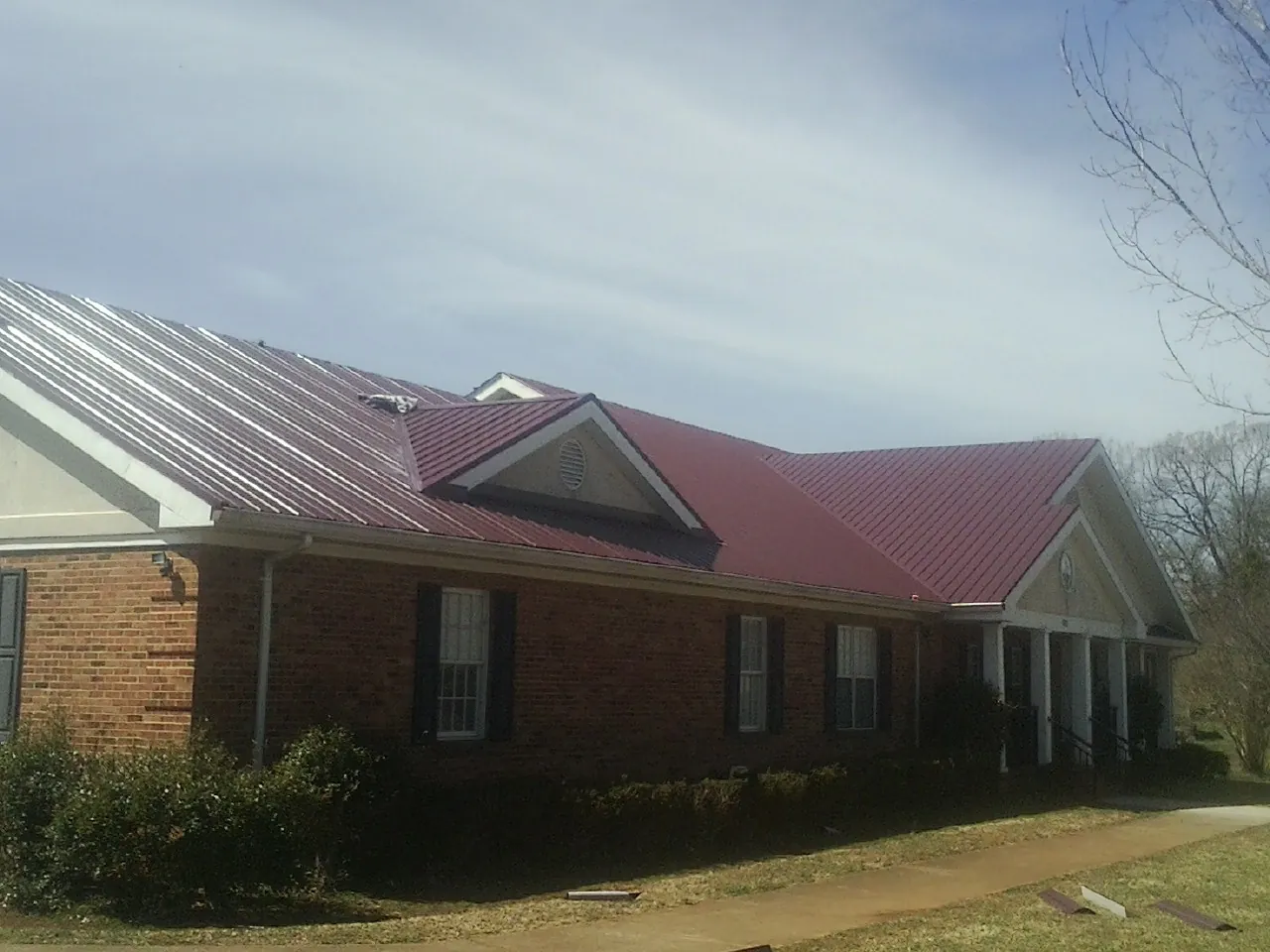 Red metal roof with gabled entries on a long brick building, from a Hail Damage Roof Repair job in West Chazy