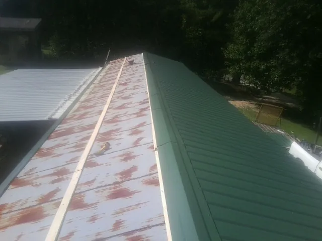 Old rusted panels beside newly installed green metal roofing — Wind Damage Roof Repair by Roofing Brothers in West Chazy