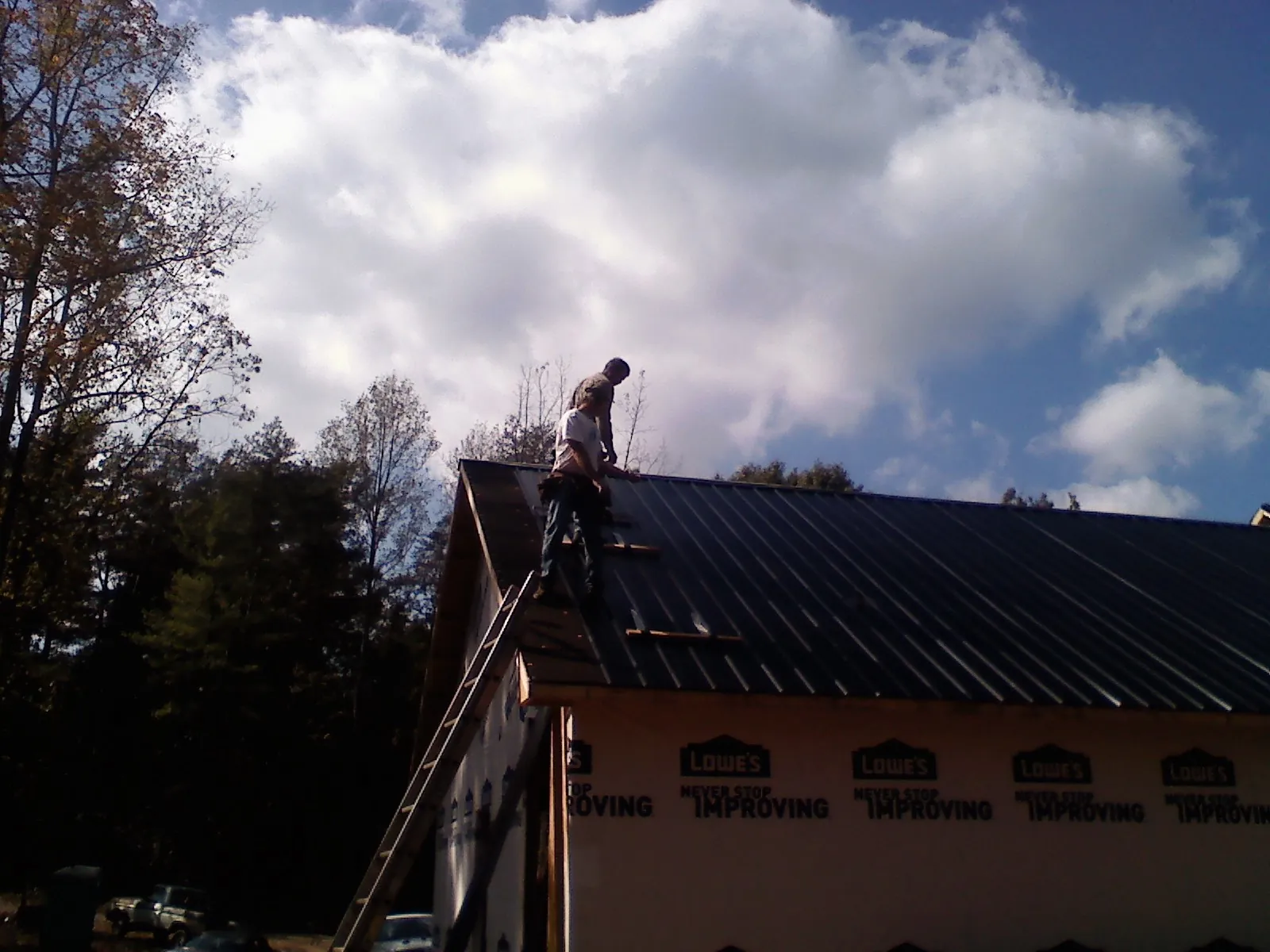 Roofer fastening dark metal panels high against a cloudy sky, from a Roof Inspection job in West Chazy