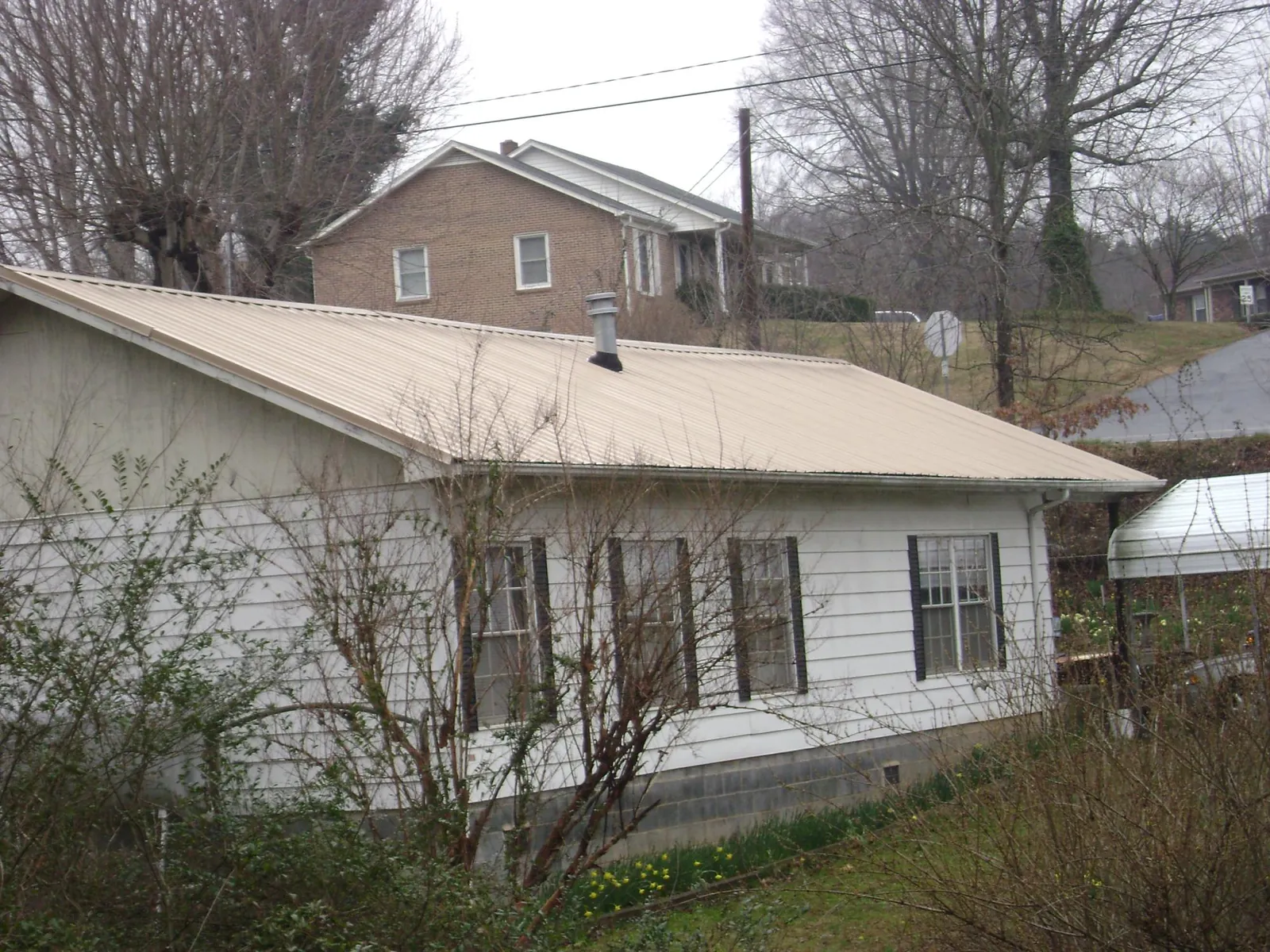 Tan metal roof on a white sided house set into a hillside — Commercial Roofing by Roofing Brothers in West Chazy